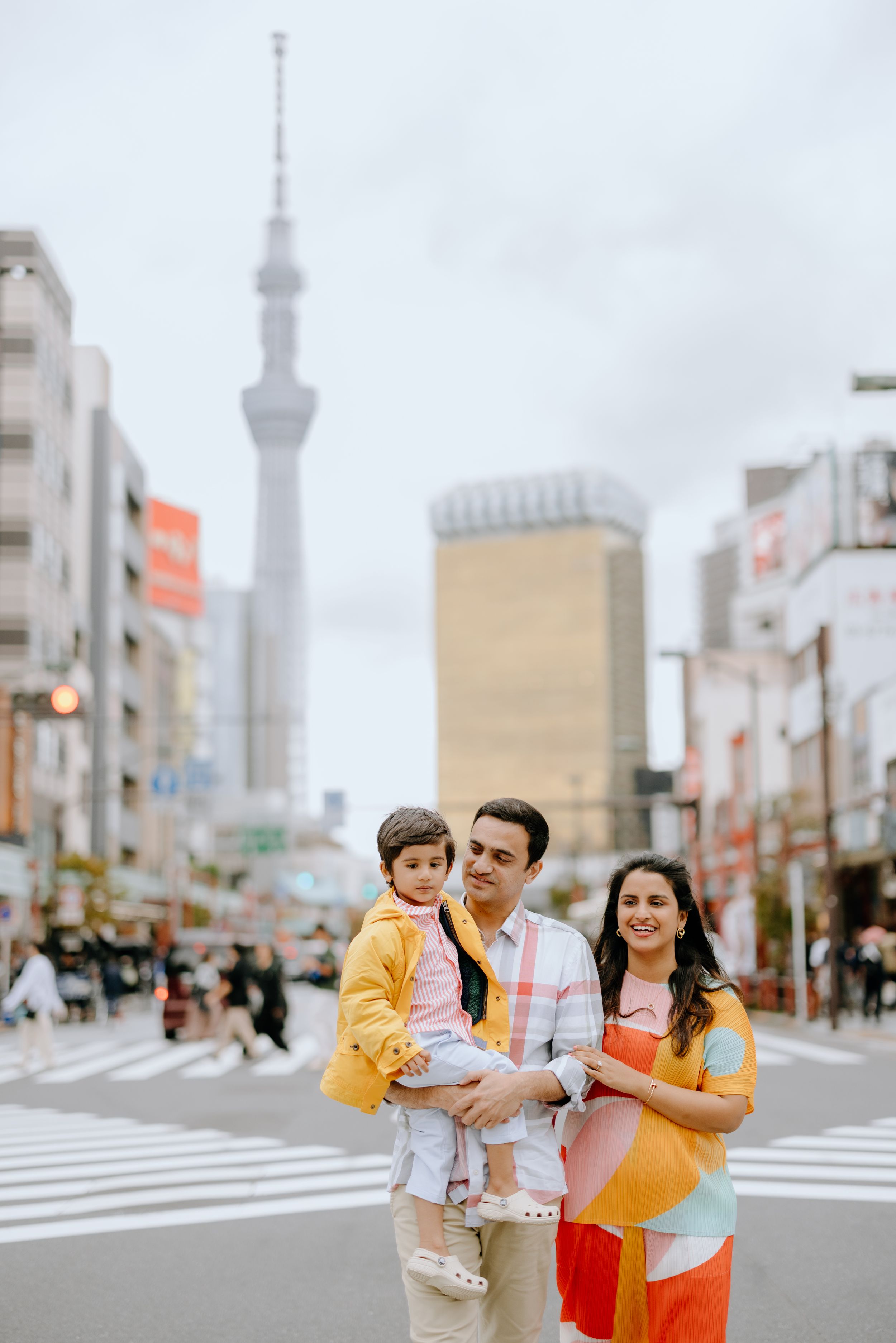 Family poses on street with Tokyo Skytree tower visible in background on cloudy day.