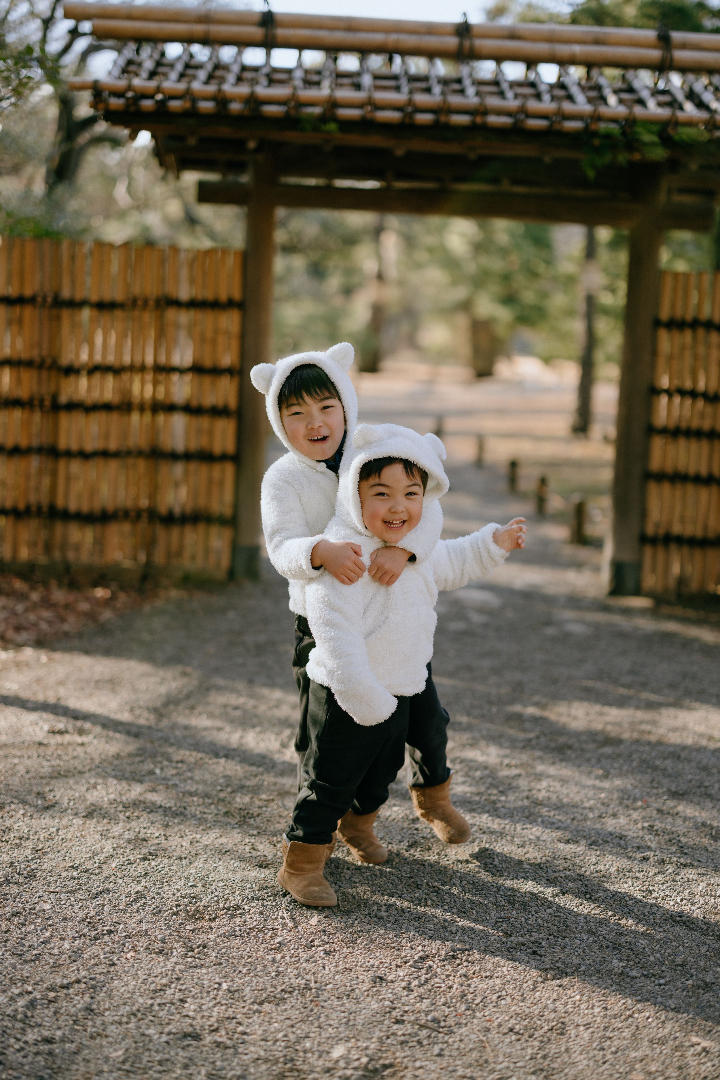 Two little boys in white outfits playing under traditional Japanese gate.