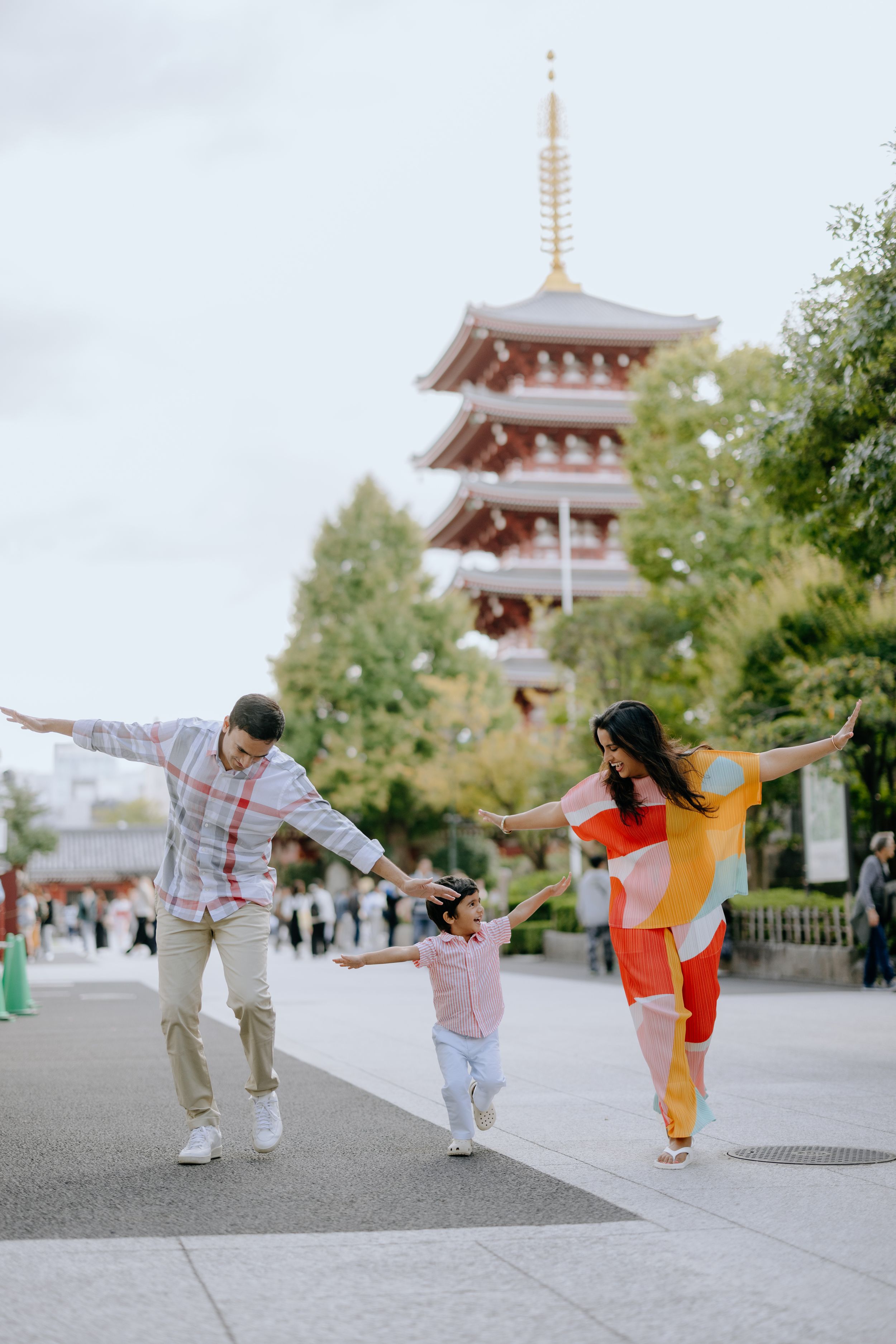 Family plays and dances together on path with traditional Japanese pagoda in background.