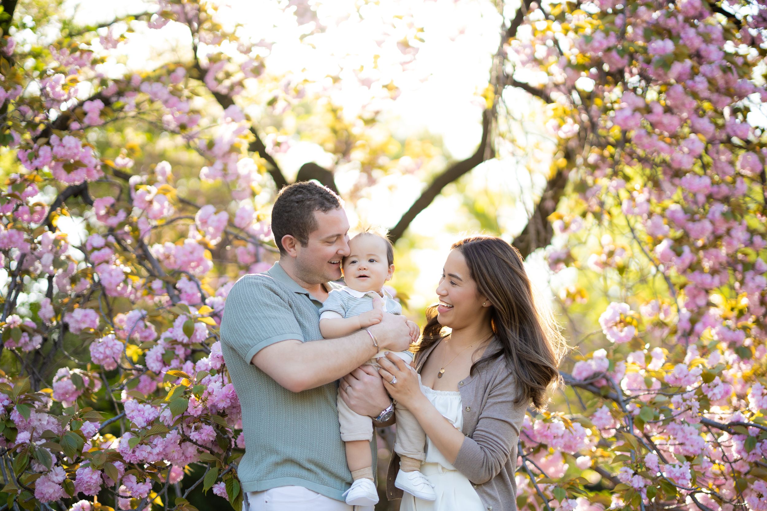 Family shares a joyful moment together under blooming pink cherry blossom trees on a sunny spring day.