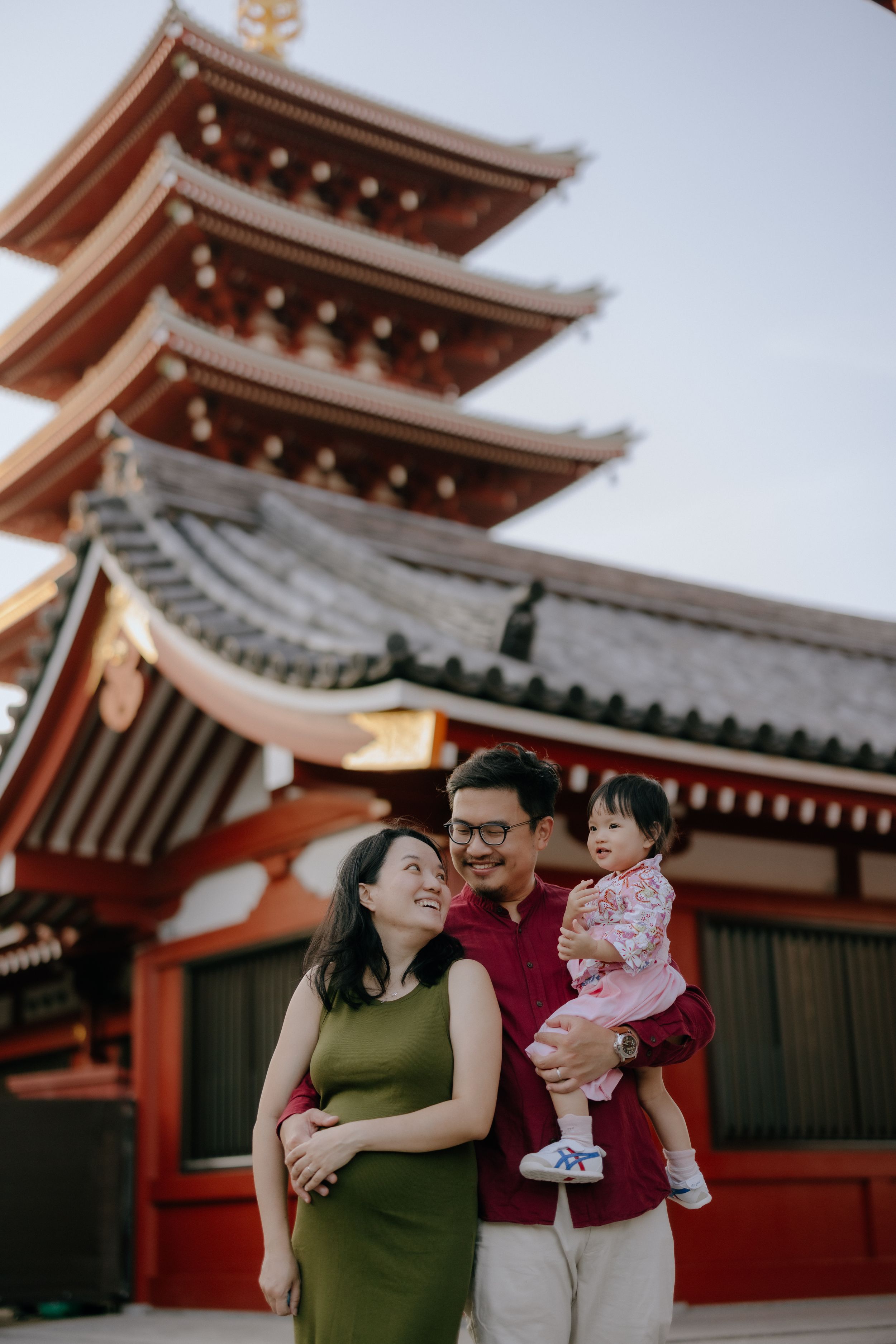 Family poses together in front of red pagoda architecture at Japanese temple during sunset.