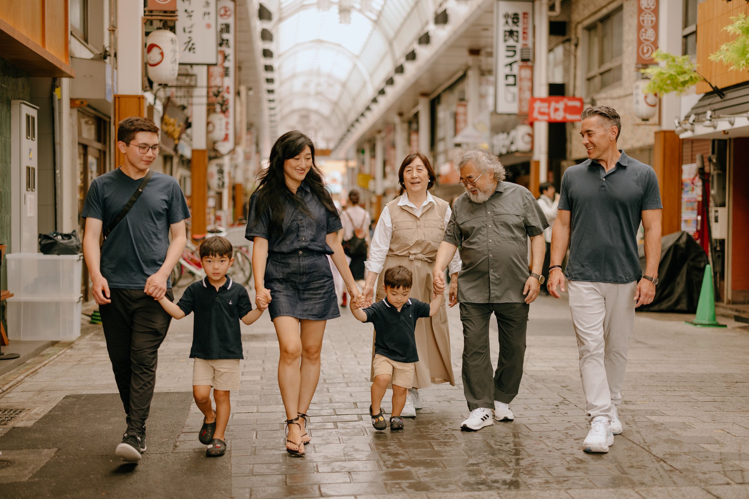 Multi-generational group walking together through a covered Japanese shopping arcade.