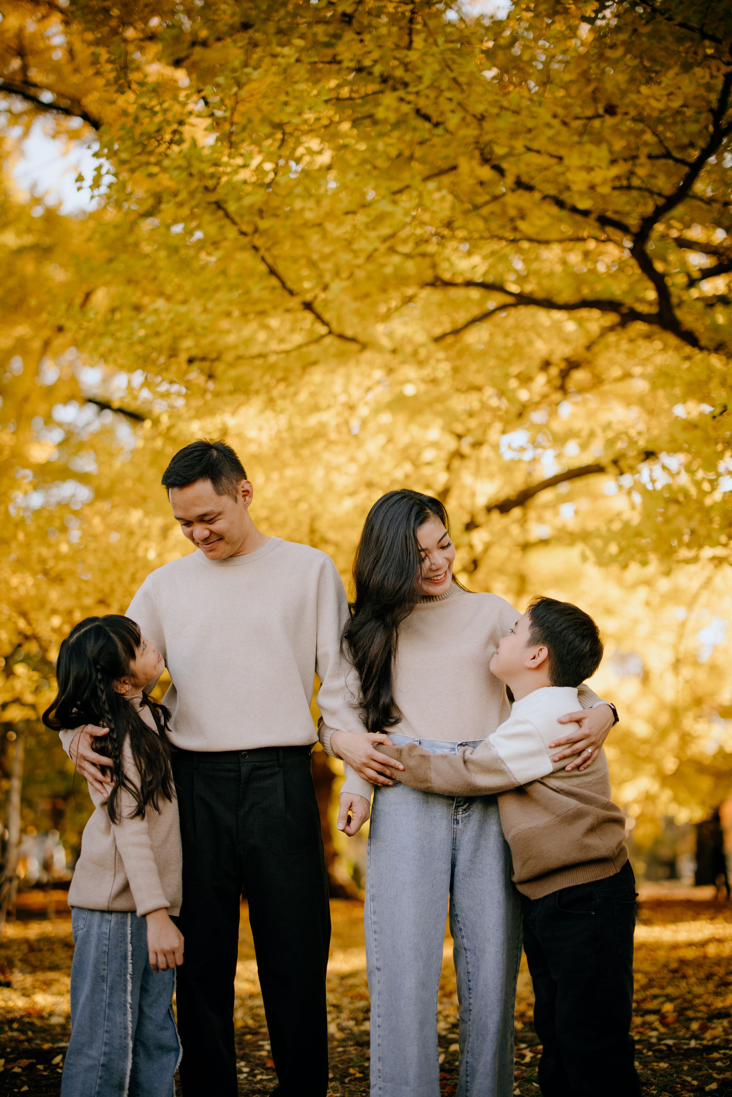 Family embracing together under golden autumn trees in the park with yellow foliage overhead.