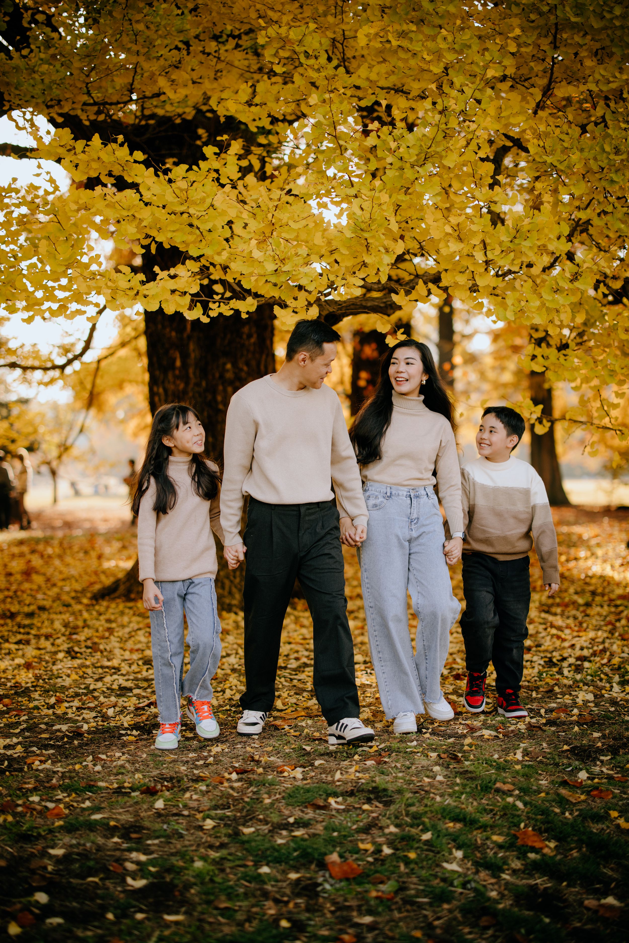 A family in matching neutral sweaters enjoys a warm autumn day beneath golden maple trees.