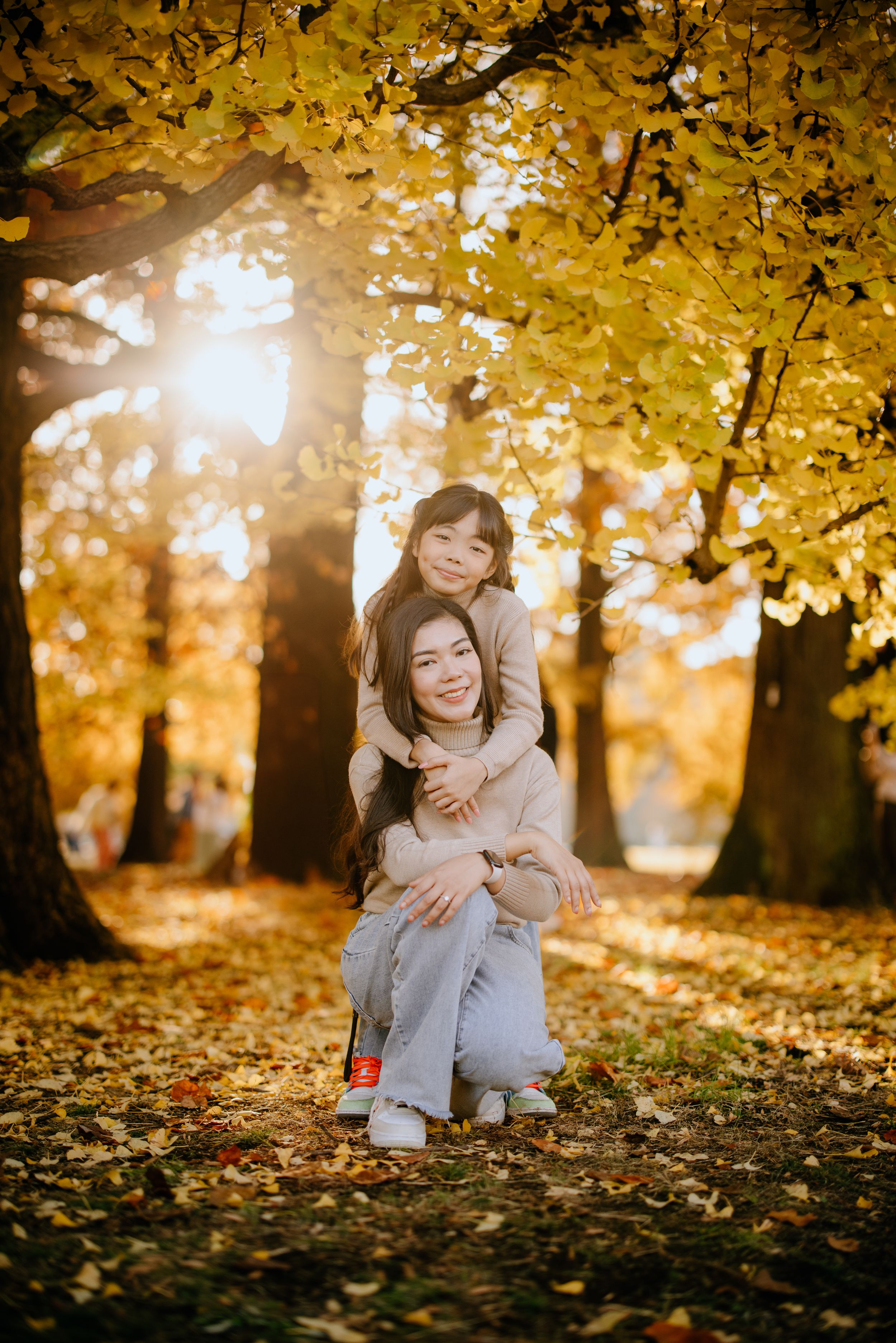 Two people sharing a tender embrace under golden autumn trees with sunlight filtering through yellow leaves in a park.