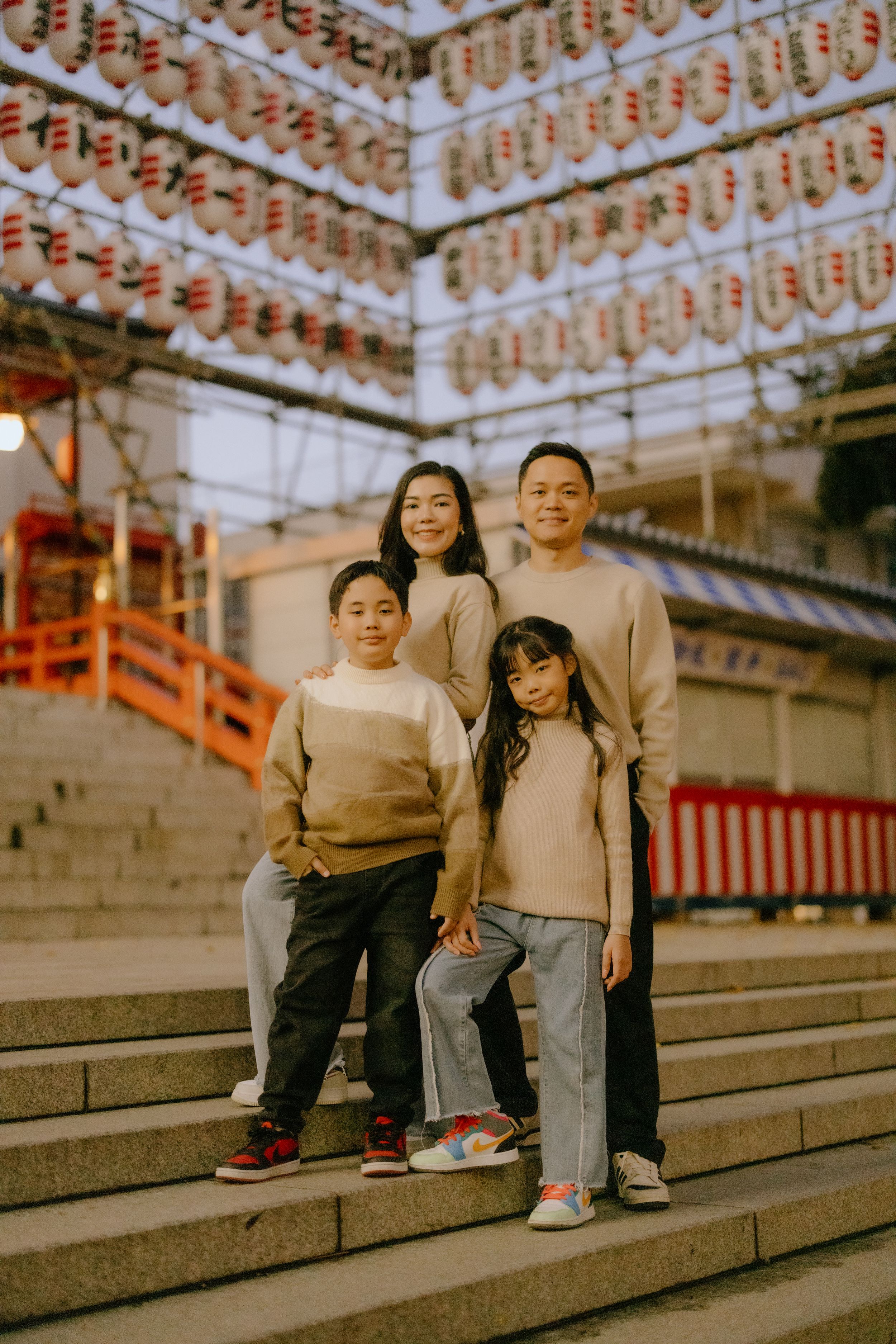 A group stands together on stone steps at a Japanese temple adorned with traditional paper lanterns in the background.