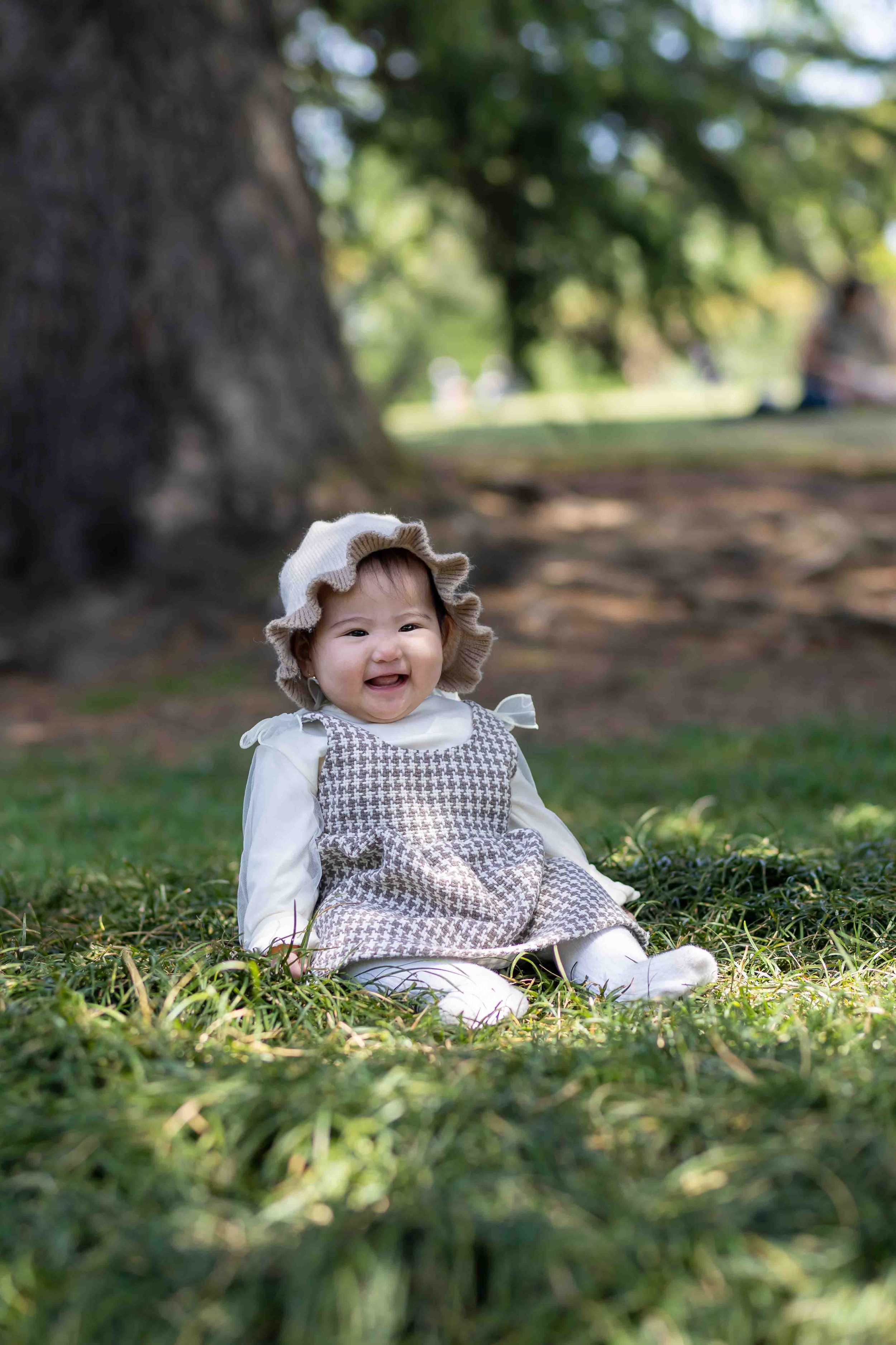 Smiling baby in vintage dress sitting on grass in a park.