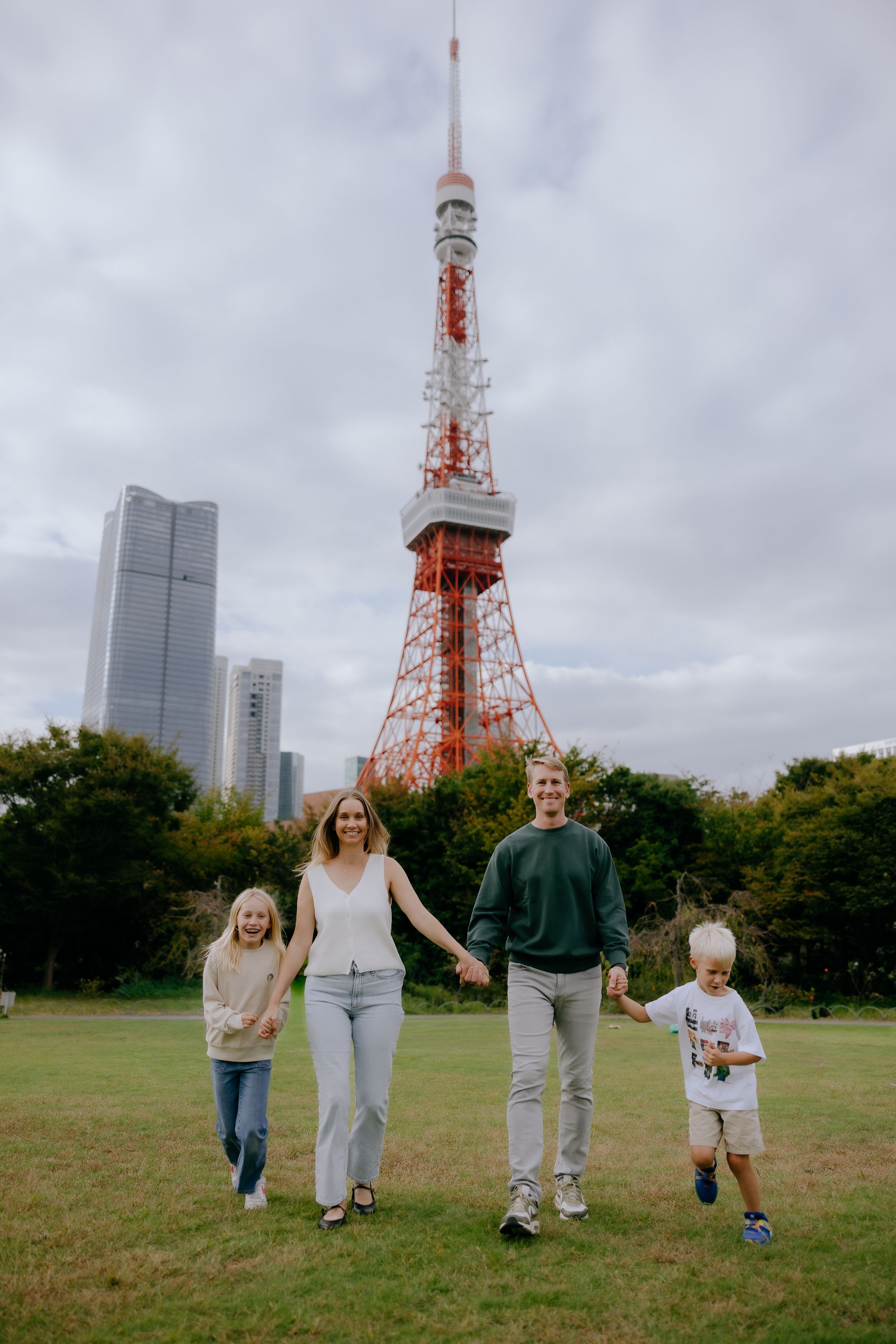 A family walks together on a grassy field with Tokyo Tower and city buildings visible in the background.