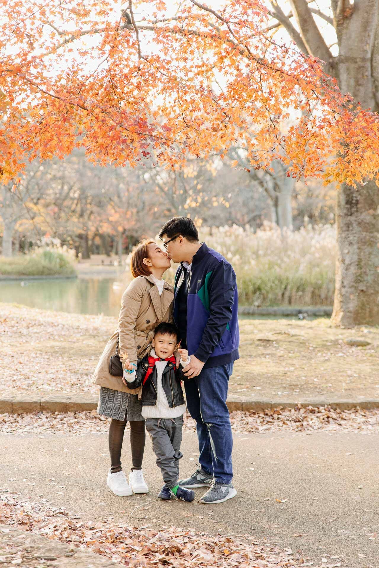 Tender family moment beneath orange autumn foliage near a lake.