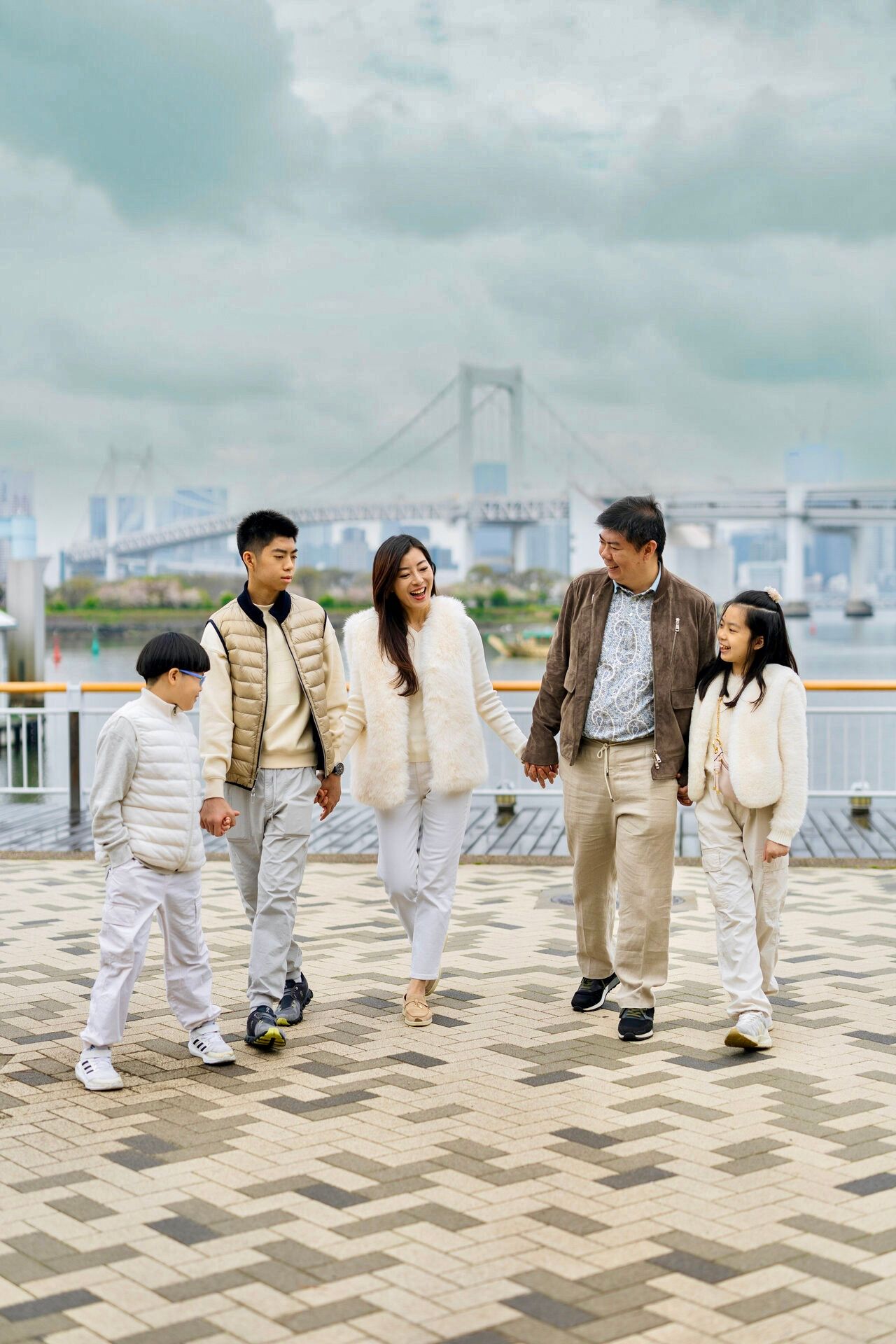 A group walking together along a waterfront plaza with Rainbow Bridge visible in Tokyo Bay.
