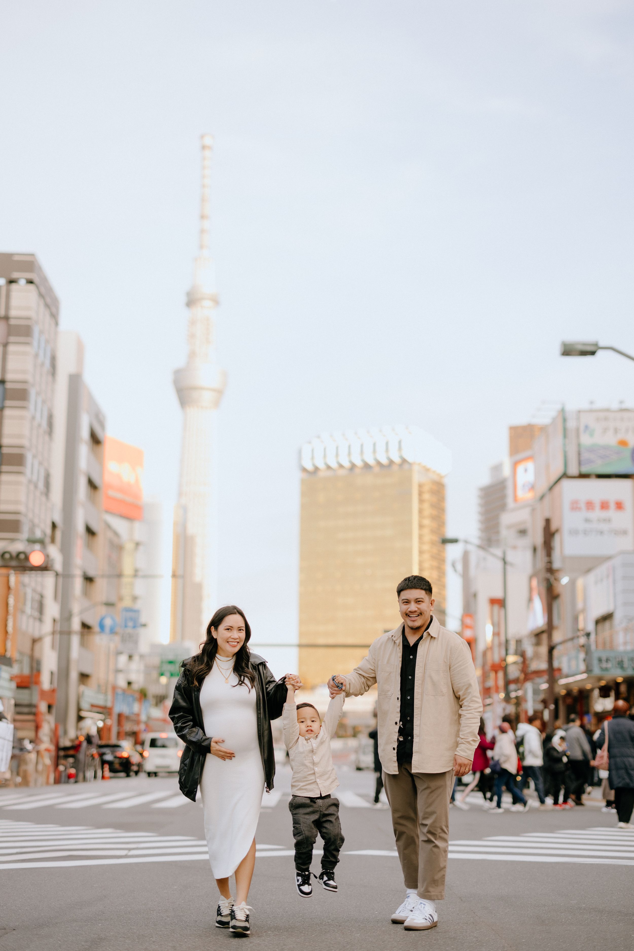 Family walking on a city street with Tokyo Skytree tower visible in the urban backdrop of Japan.