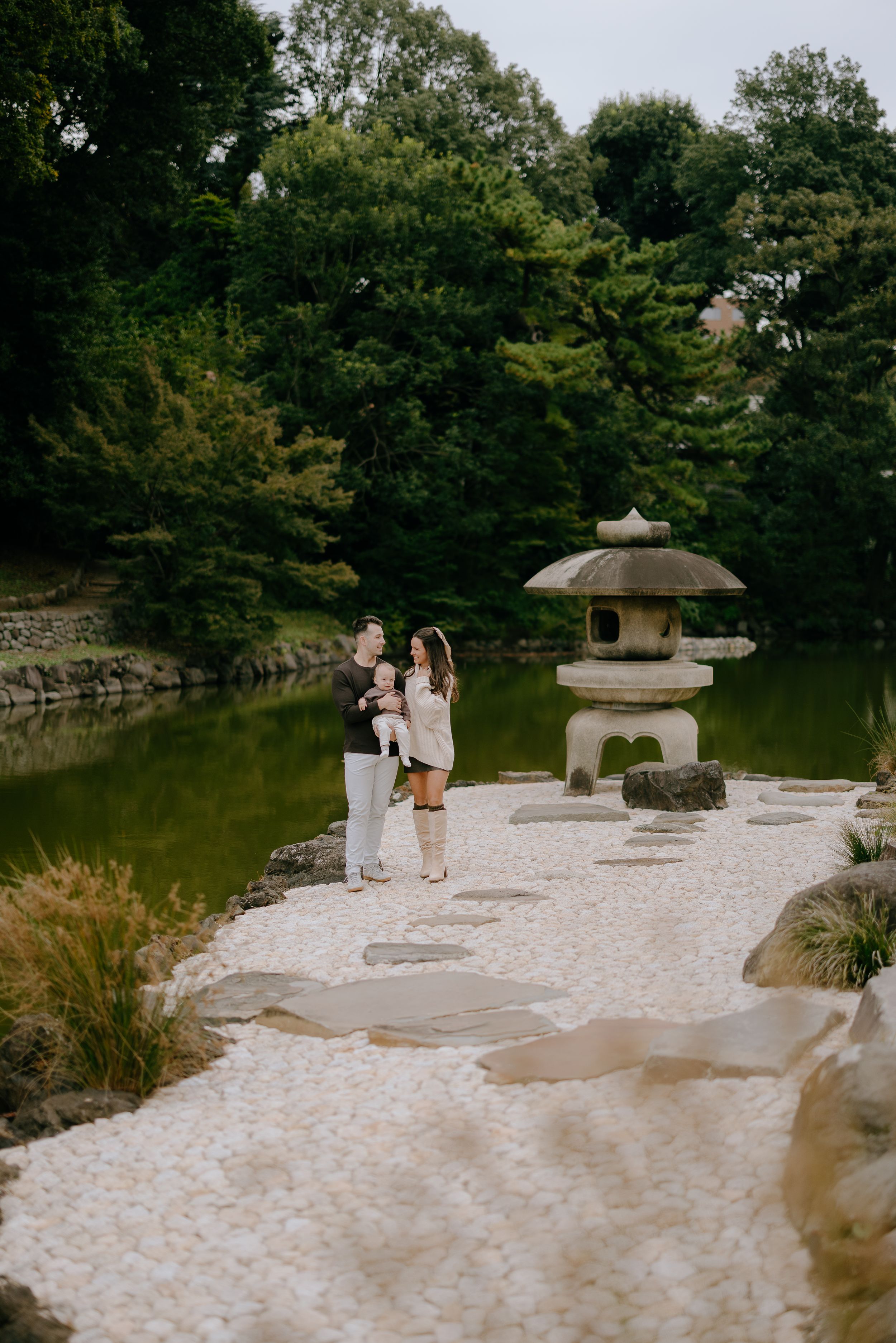 A peaceful Japanese garden with a stone lantern and pond surrounded by lush greenery and white gravel paths.