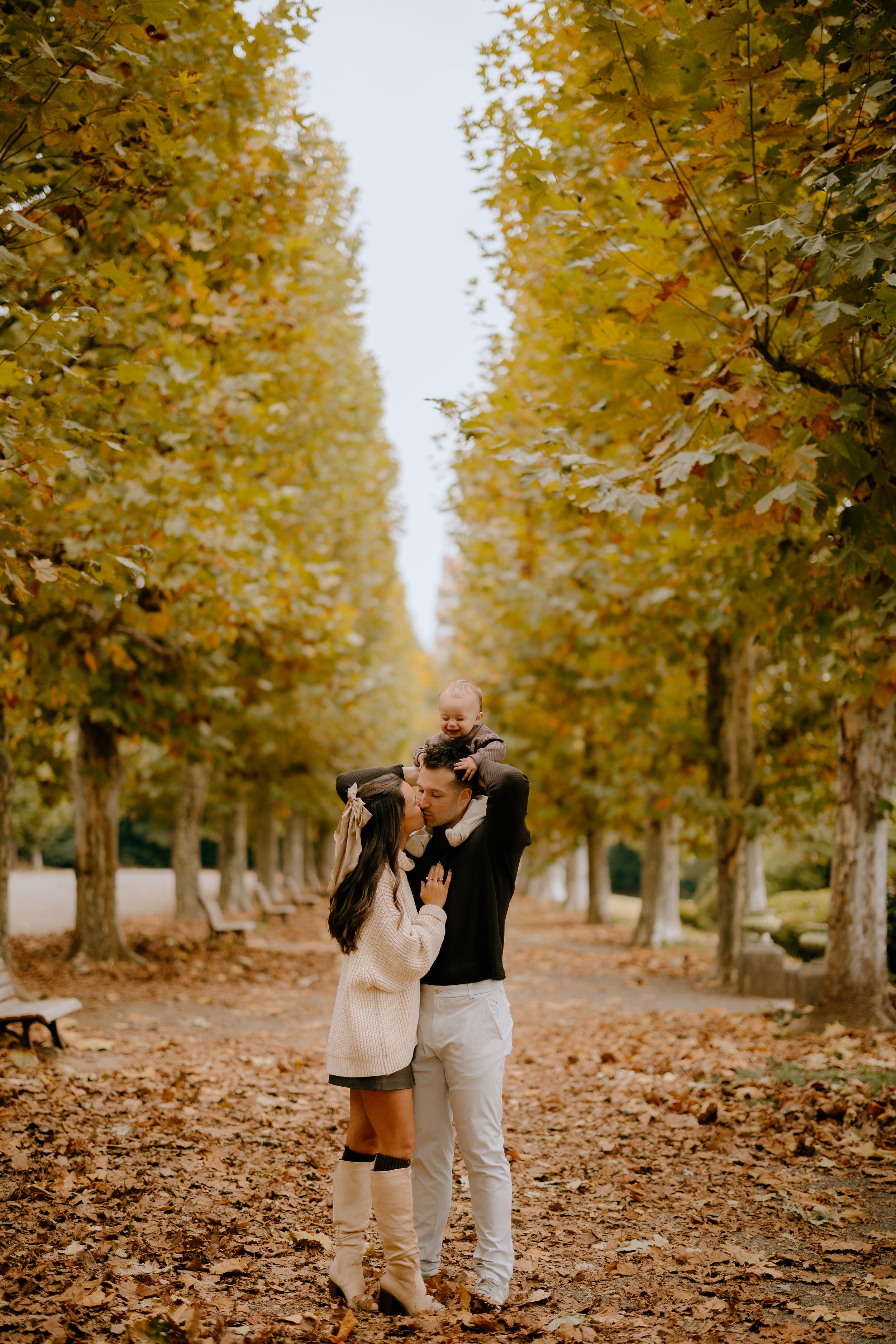 A couple walks through a golden autumn tree-lined path covered in fallen leaves on a romantic fall afternoon.