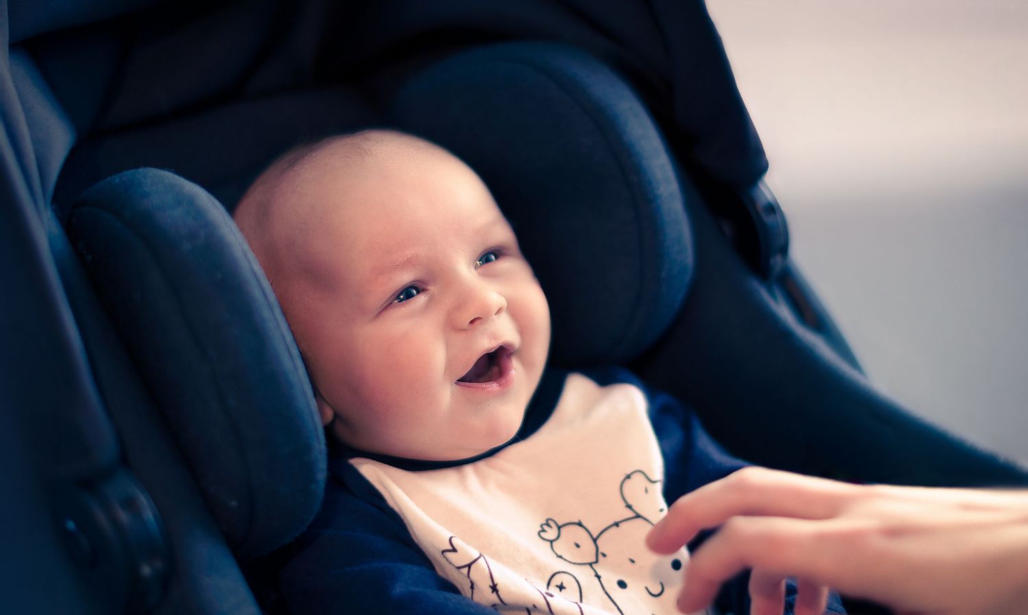 Happy baby laughing while sitting in a navy blue car seat.
