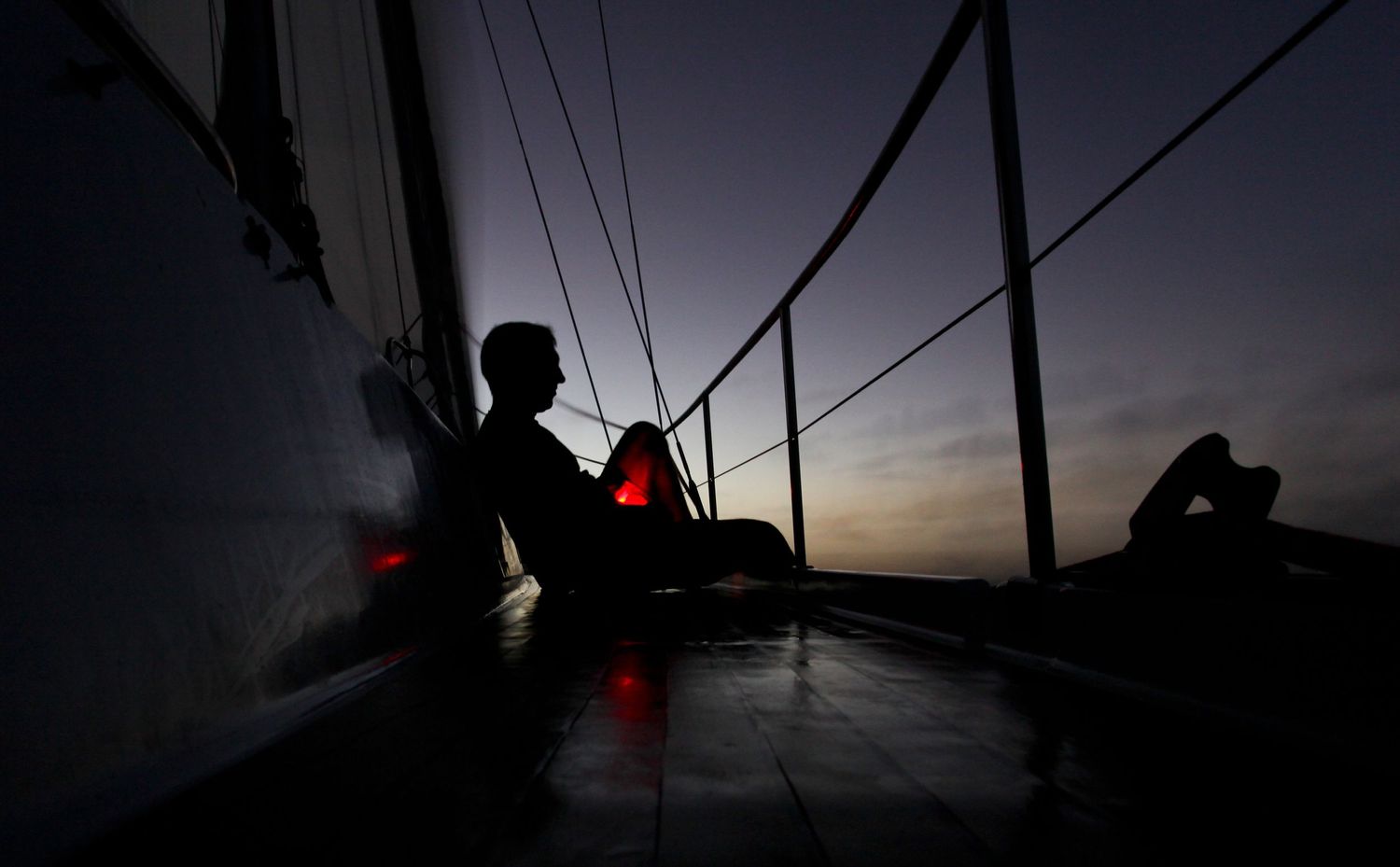 Silhouetted figures on sailboat deck during dramatic sunset.