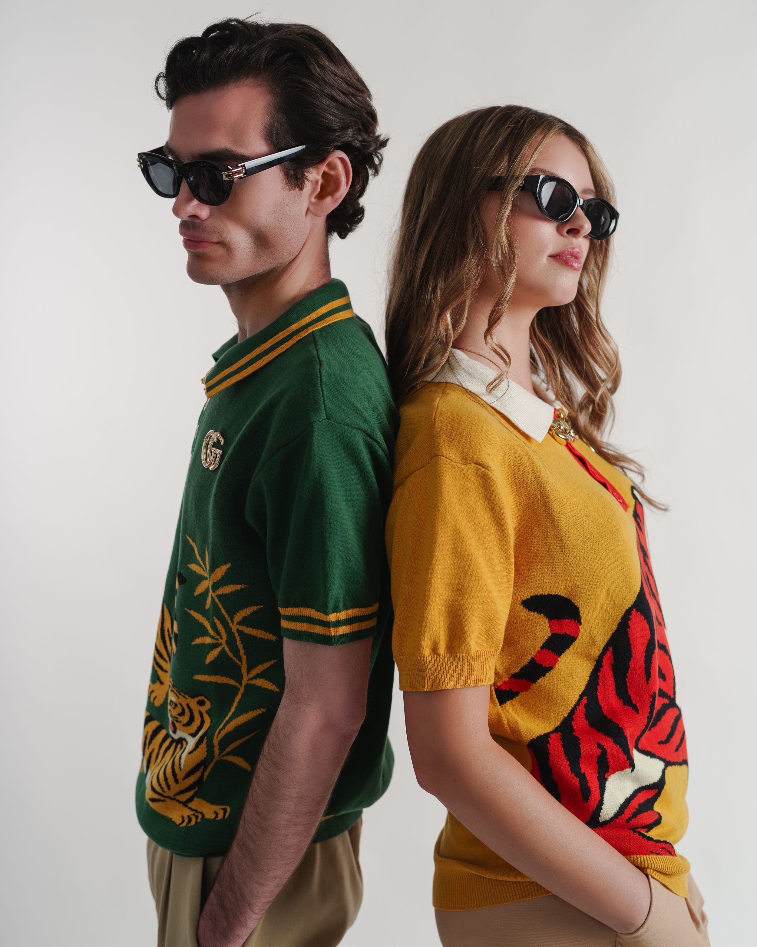 Two models in Gucci tiger-print polo shirts, green and yellow, wearing sunglasses, posing back-to-back.