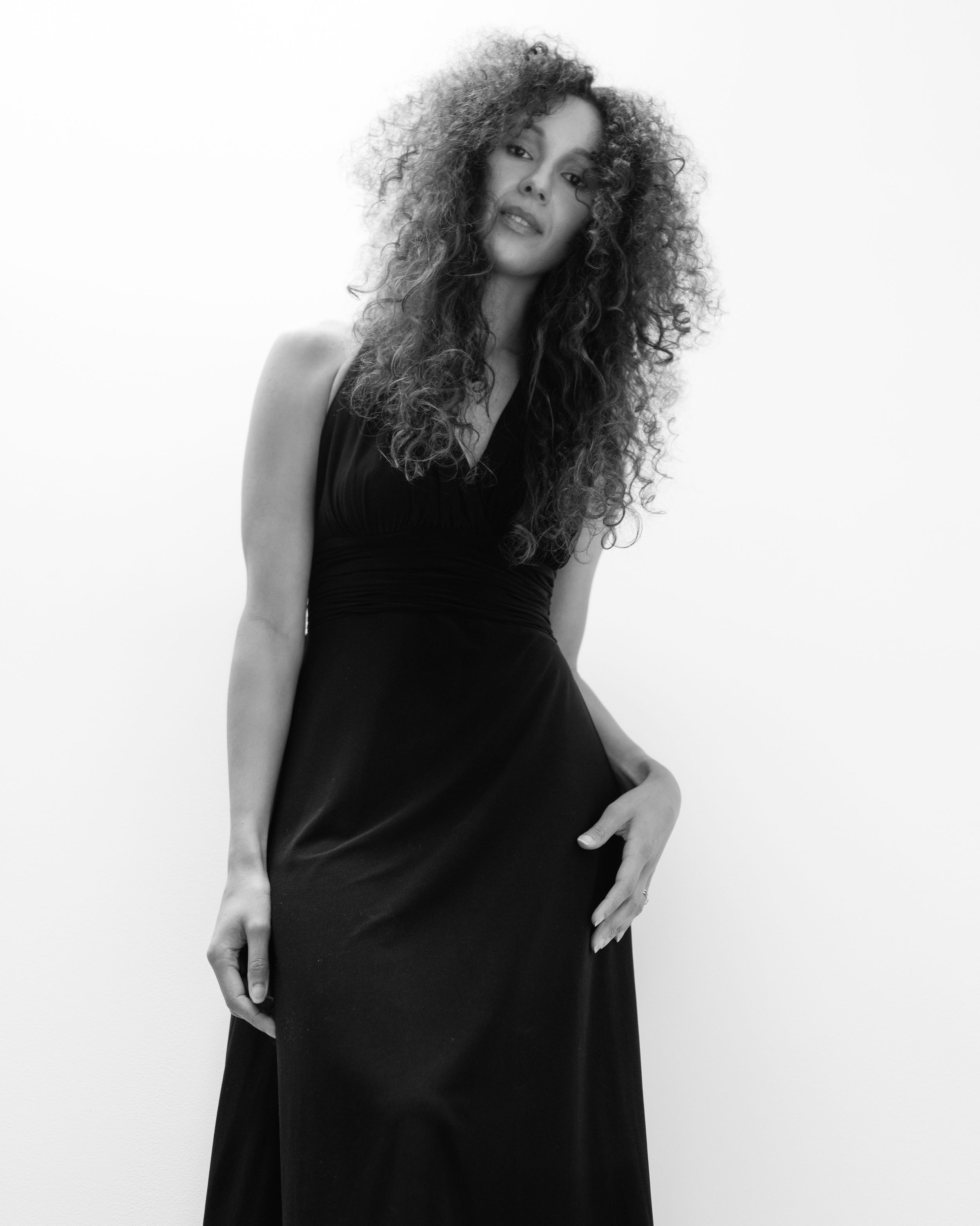 A black and white portrait featuring long curly hair and a flowing black dress against a white background.