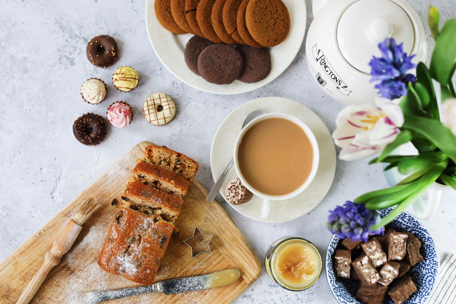 Chocolate cookies and biscuits arranged on a plate with tea and purple flowers in the background.