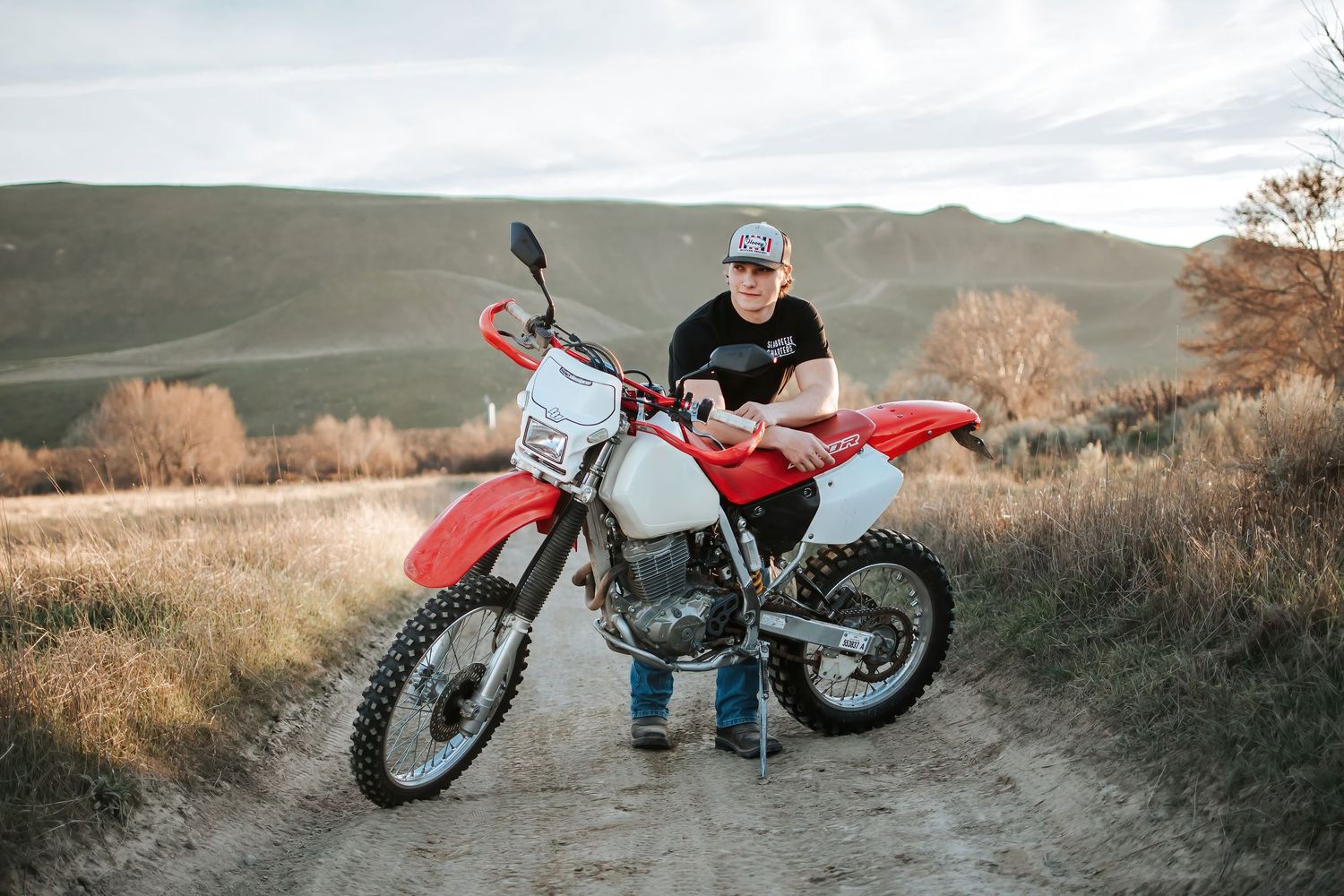 Senior sitting on red dirt bike motorcycle against rolling hills landscape at Hover Park in Kennewick, Washington.