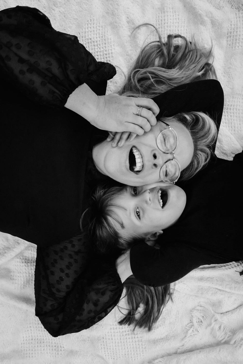 Two people lying down and laughing together in a black and white portrait.