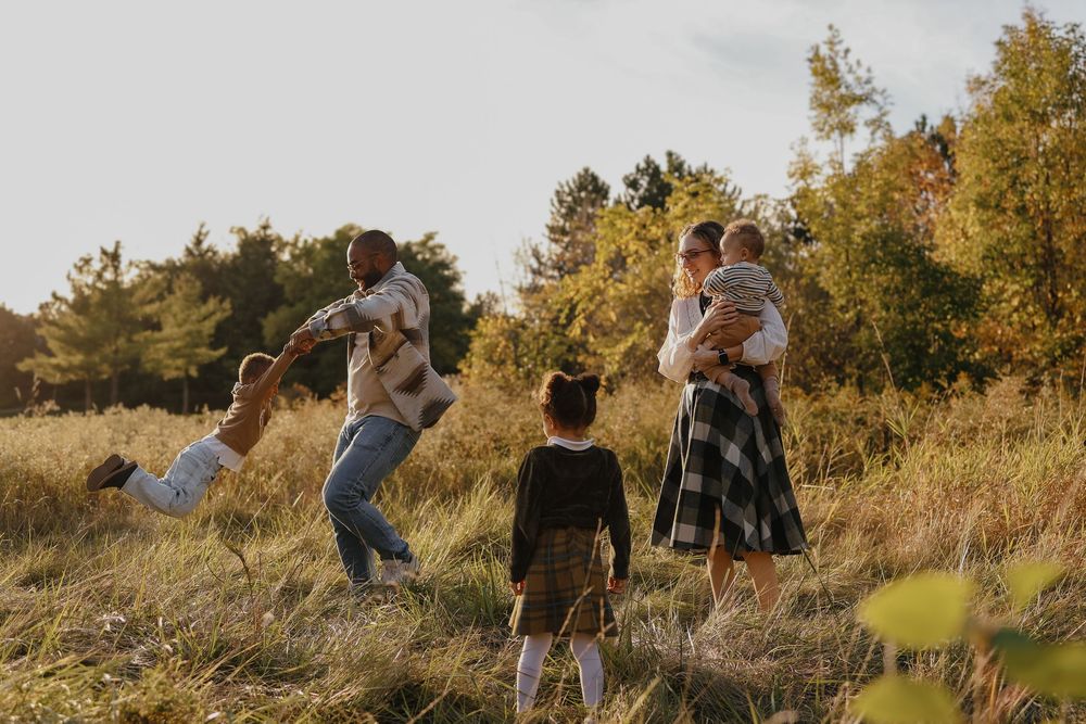 Group of people walking through tall grass and autumn trees during golden hour sunset in a field.