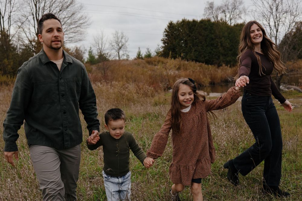 A group of people holding hands while walking together through a grassy field on an autumn day.