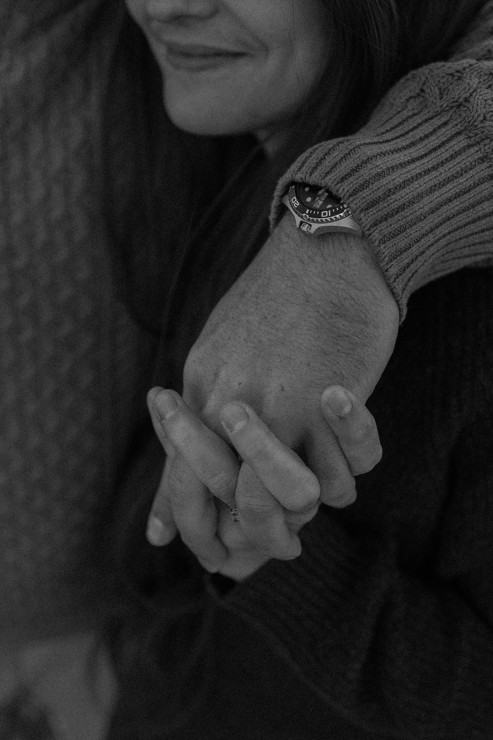 Black and white closeup of clasped hands with a decorative ring on the sleeve of a ribbed sweater.
