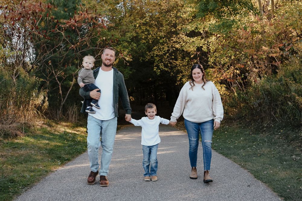 Family walking together hand in hand on paved trail surrounded by autumn foliage.