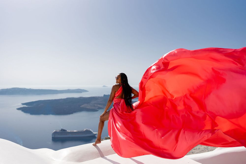 Flowing red dress contrasts against white Santorini architecture overlooking the caldera.