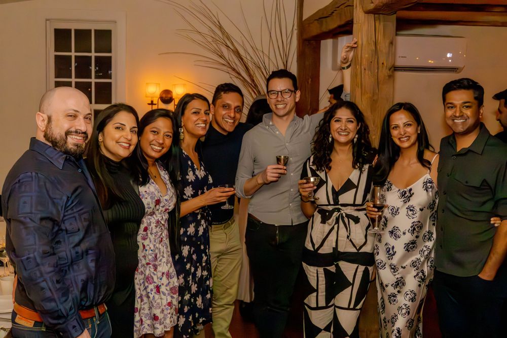 Group of friends pose together at an indoor party with warm lighting.
