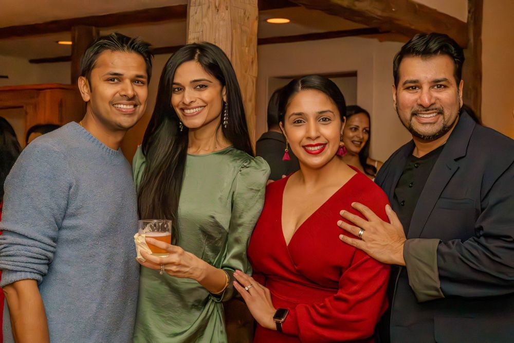 Four friends smile together at an indoor gathering.