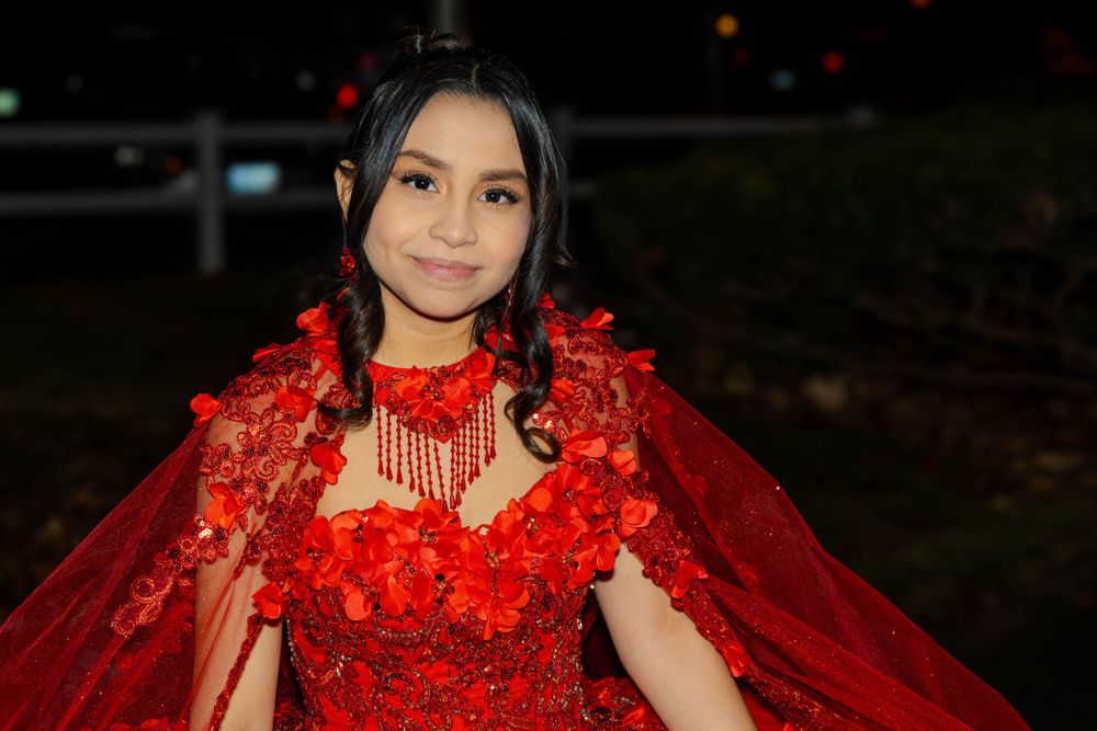 Celebrant wearing an ornate red gown with cape and matching floral accessories at an evening event.