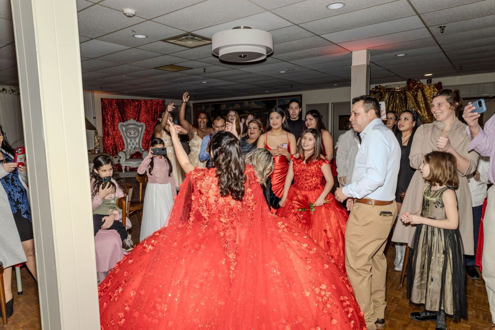 Celebration scene showing dancers in red dresses among party guests in an indoor venue.