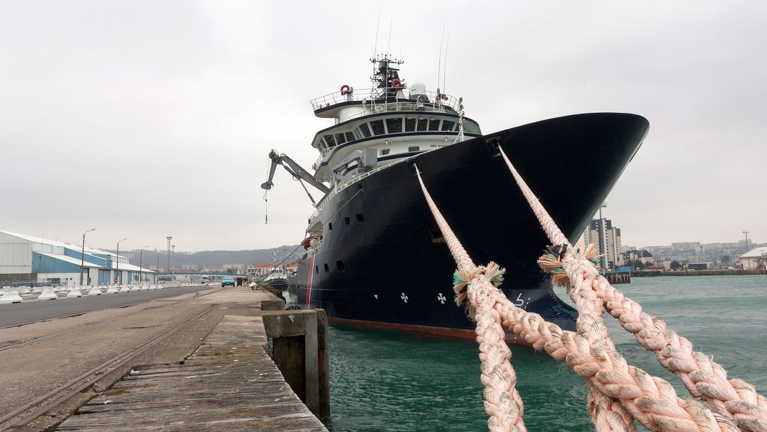 Large industrial ship moored at dock with thick mooring ropes visible in foreground.