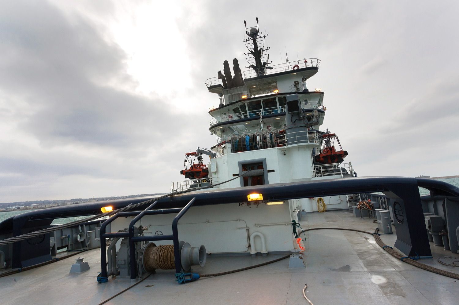 Modern ship's bridge and navigation equipment viewed from deck under overcast sky.