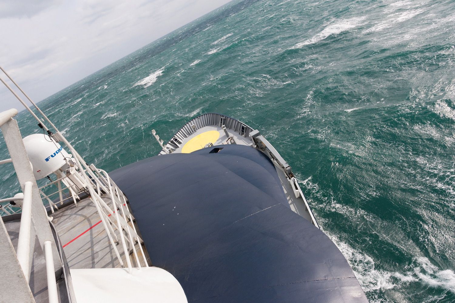 Ship's bow cutting through rough seas with waves visible from elevated deck position.