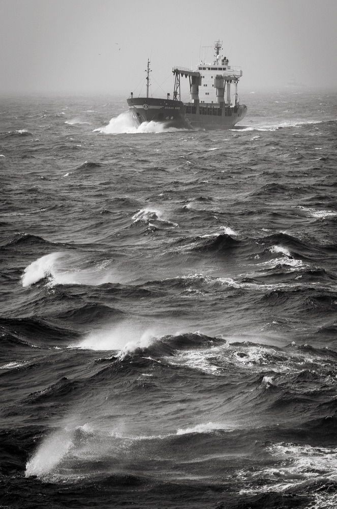 Cargo ship battles rough seas with large waves in stormy black and white conditions.