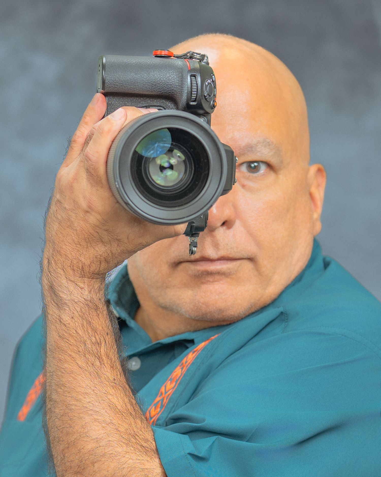 Portrait of photographer holding professional camera outdoors in blue jacket.