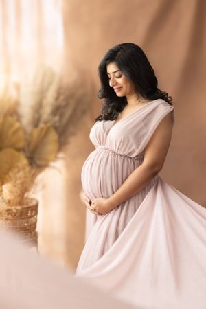 Maternity portrait with woman in flowing pink dress against warm toned background.