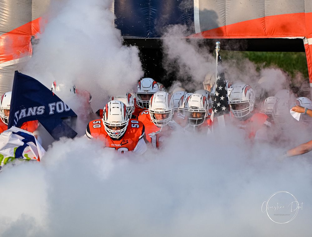 Football team running through smoke and banners during game entrance.