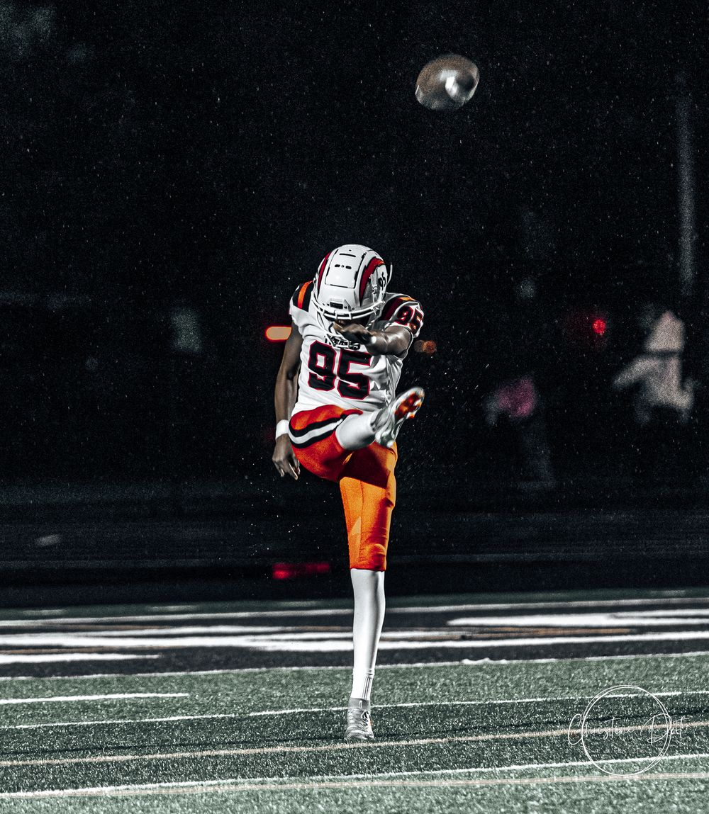 Football player punting the ball under stadium lights at night.