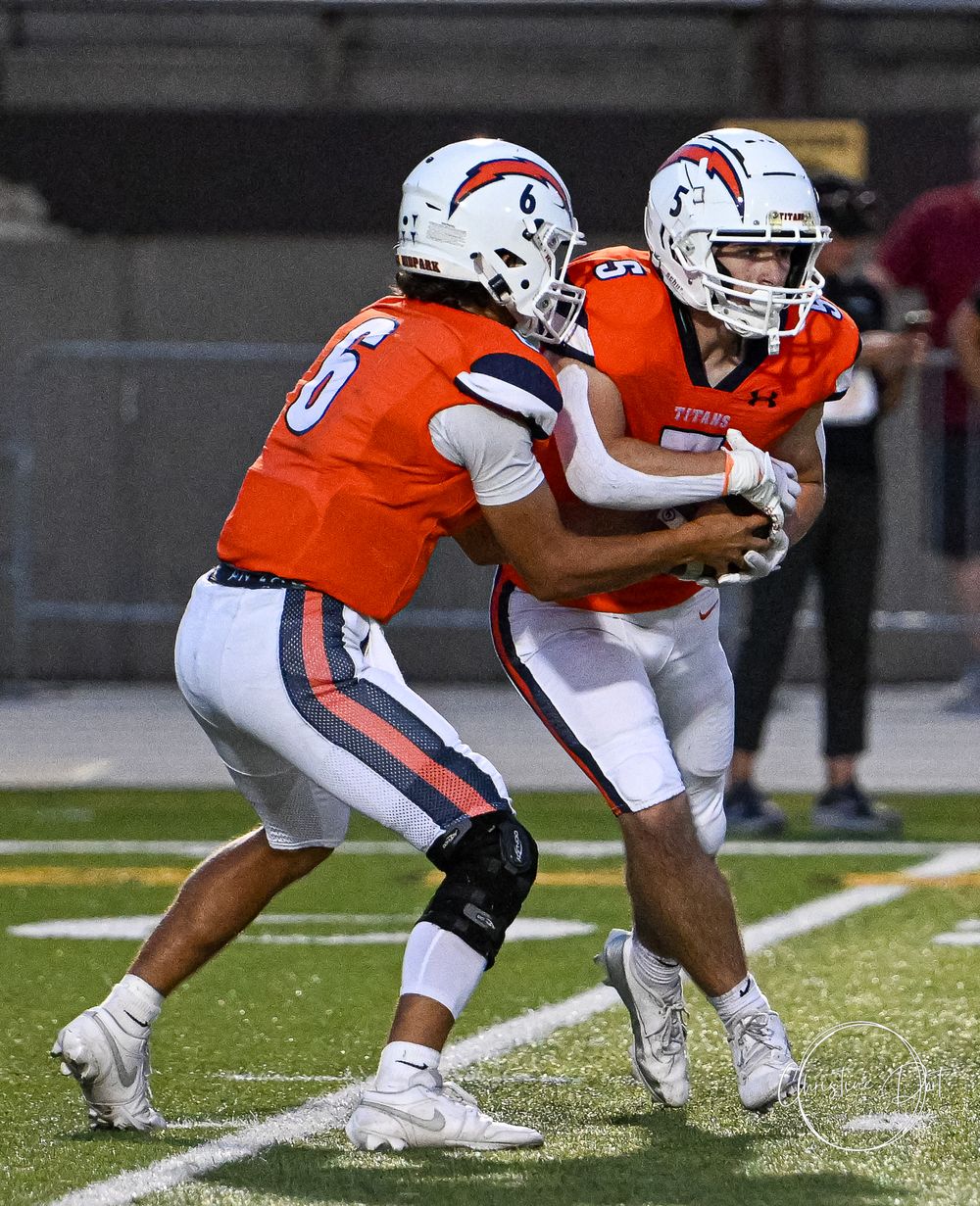 Football players executing a handoff play in orange uniforms during a game.