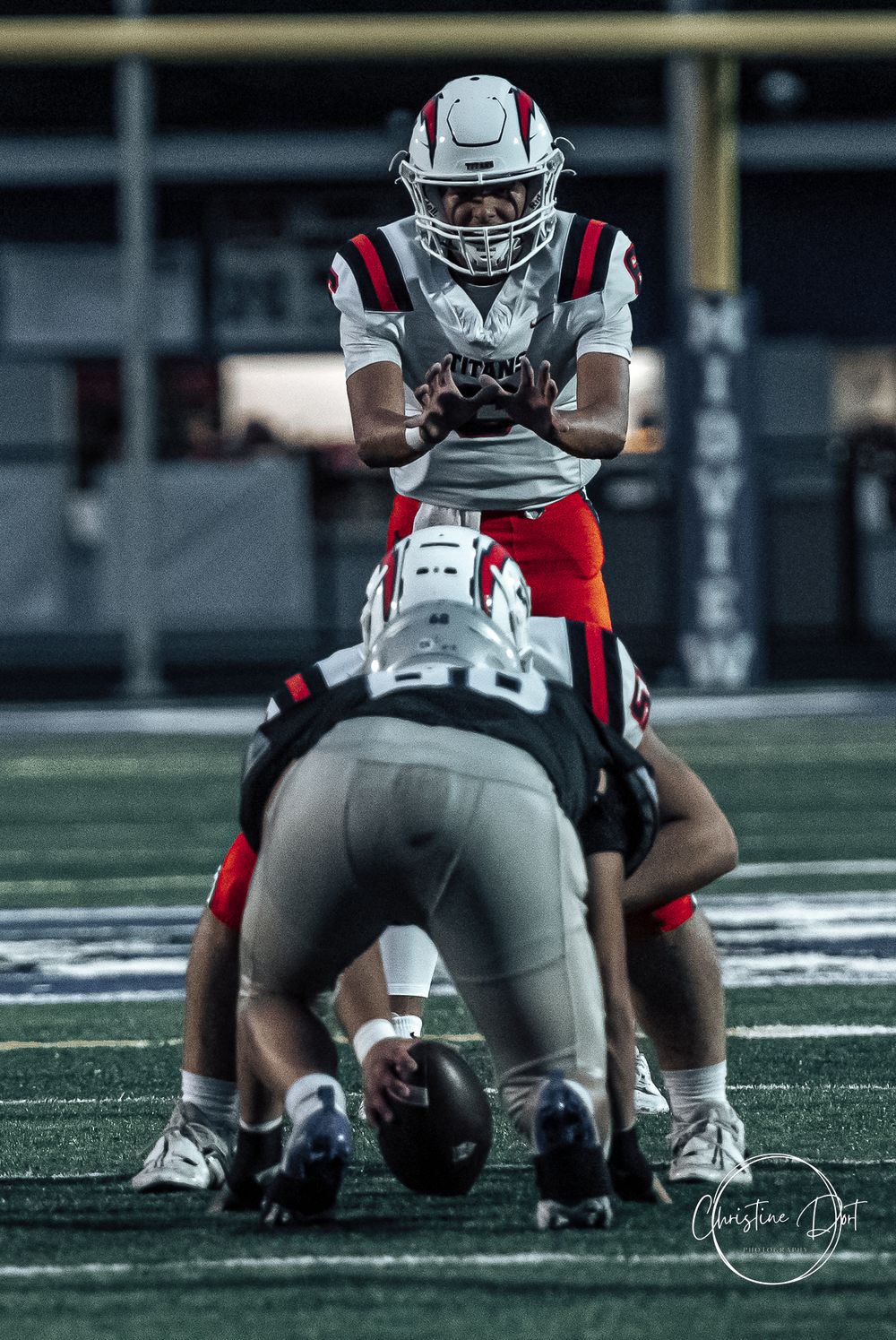 Football player taking snap from center during nighttime game.