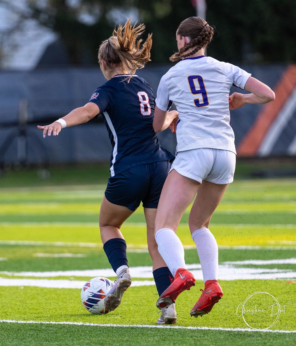 Soccer players from opposing teams battle for possession of the ball on athletic field.