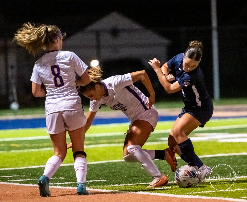 Soccer players dive and compete for control of the ball during an intense match.