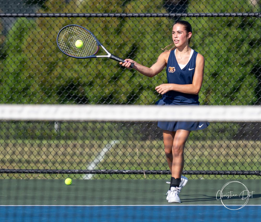 Tennis player executing a forehand shot on a blue outdoor court on a sunny day.