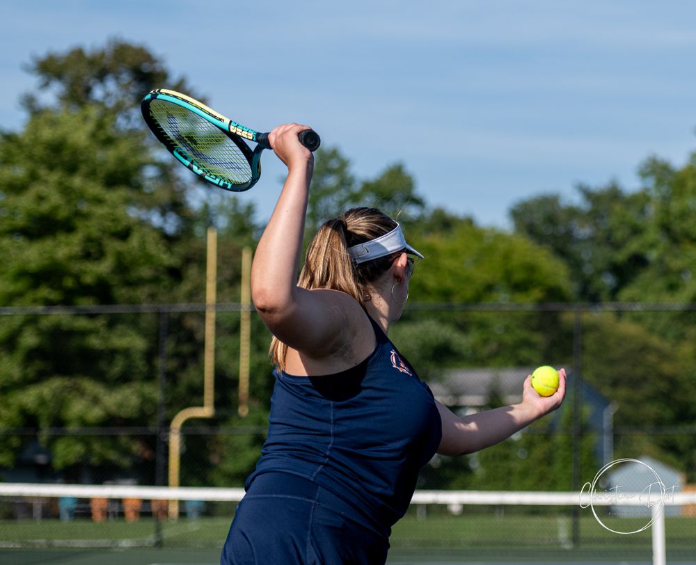 Tennis player preparing to serve with ball toss on outdoor court.
