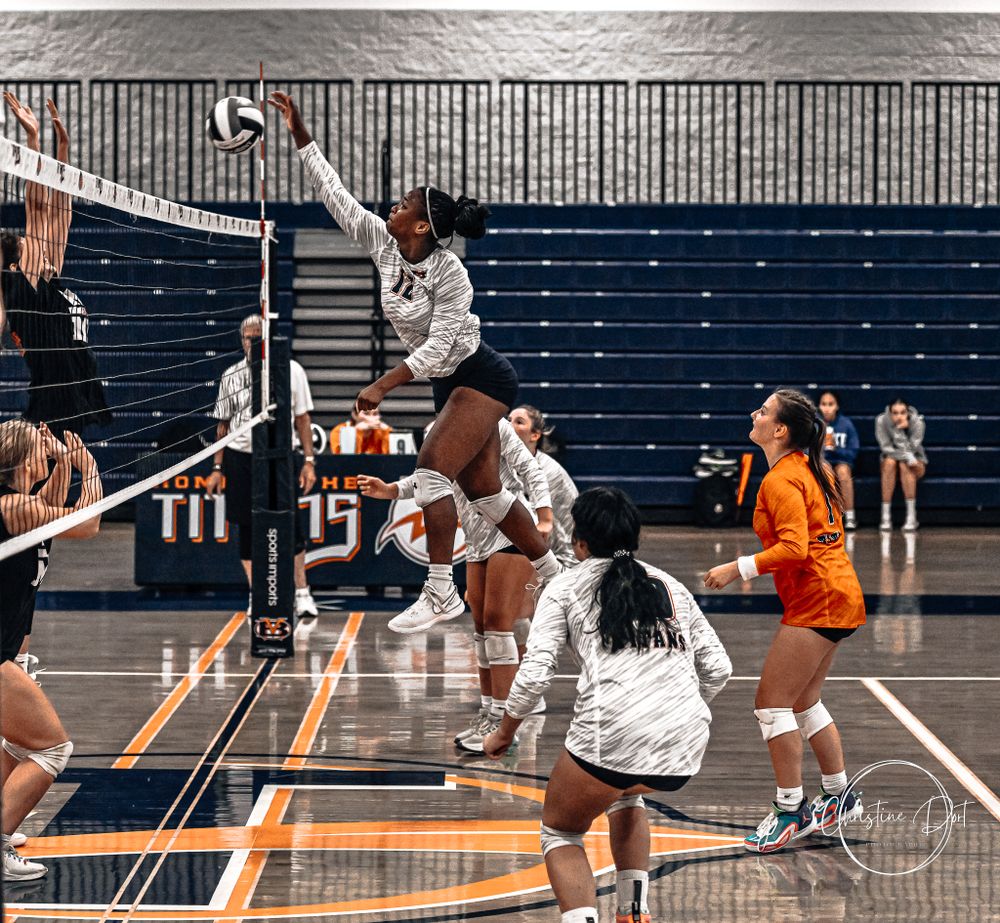 Players jumping at the net during an intense volleyball match in a gymnasium.