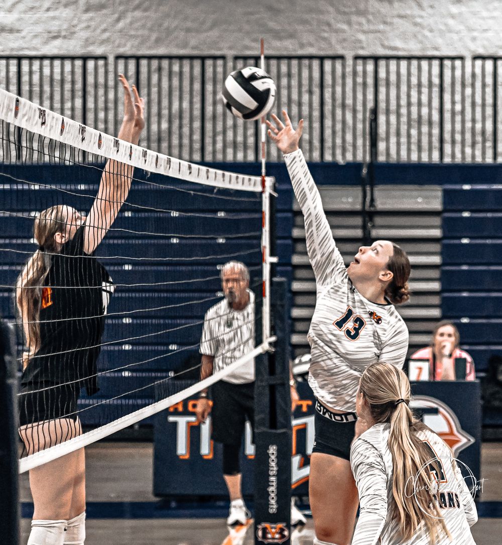 Two volleyball players competing at the net for a point during an indoor game.