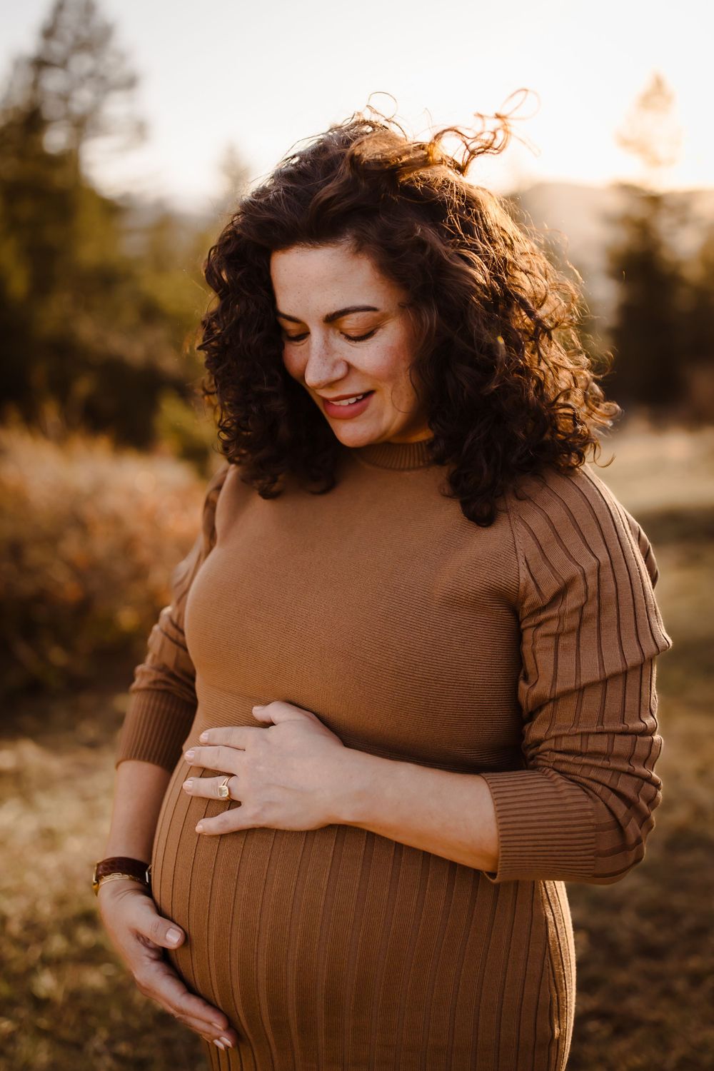 A pregnant mother smiles gently while cradling her baby bump at golden hour in Denver